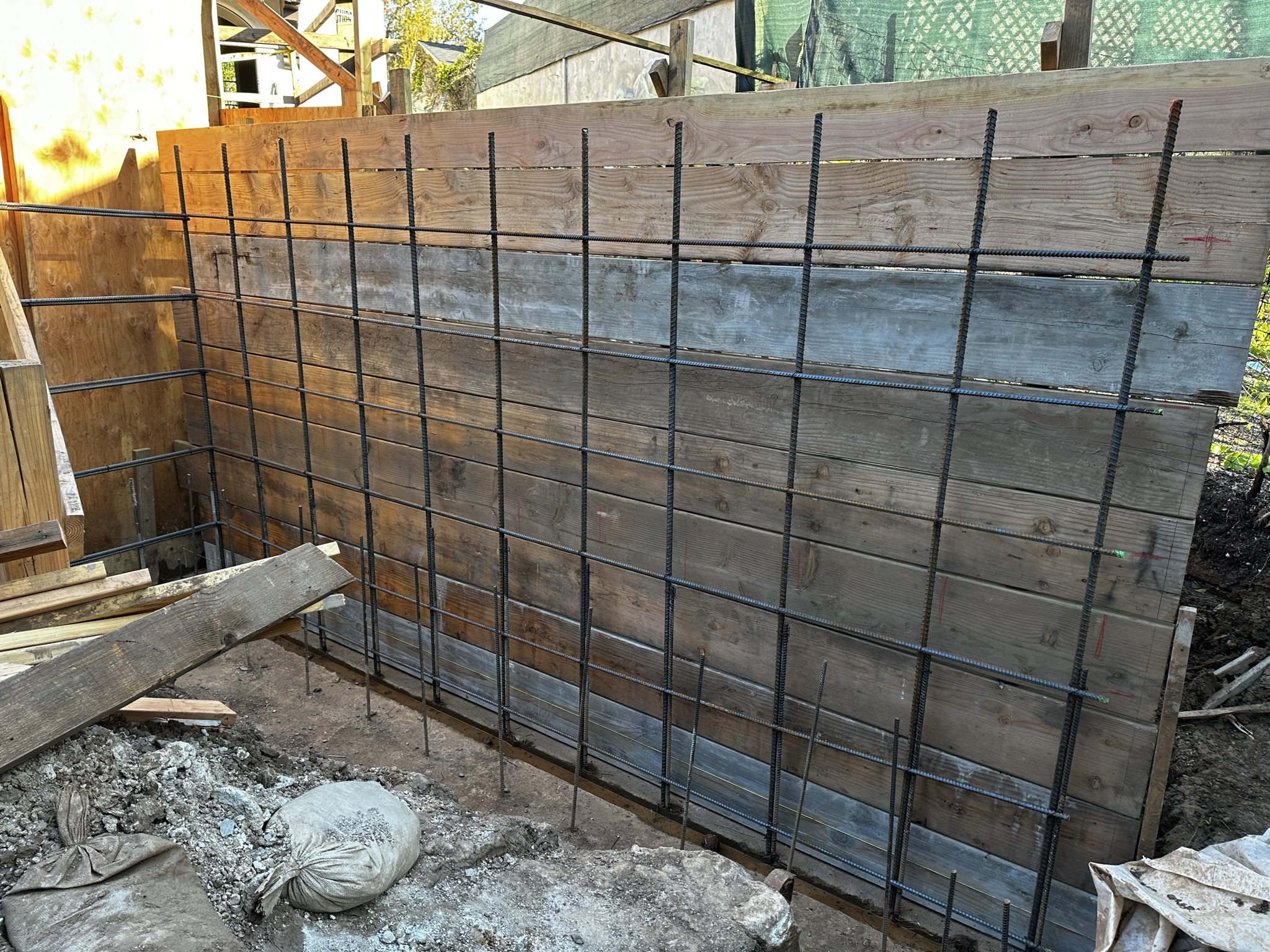 A construction site showcasing a wooden framework with rebar grid reinforcement for a retaining wall, prepared for concrete pouring.